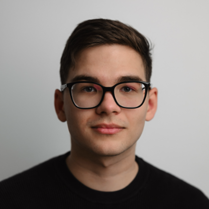 Portrait of a young man with dark hair wearing black glasses.